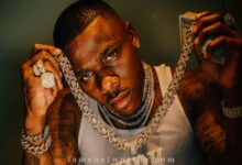 DaBaby showing his diamond "KIRK" chain, luxury jewelry, and cash for net worth 2025 banner image.