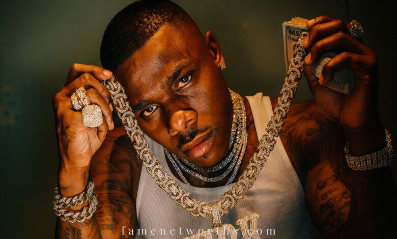 DaBaby showing his diamond "KIRK" chain, luxury jewelry, and cash for net worth 2025 banner image.